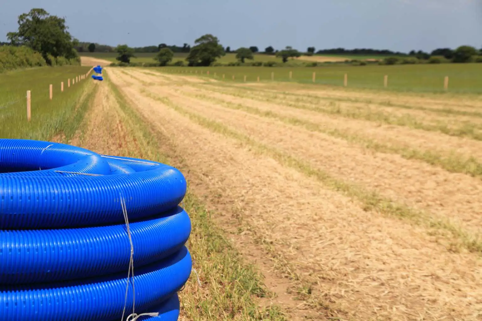 Blue drainage pipes laid along a rural track supporting cross-country utility routes, demonstrating land drainage