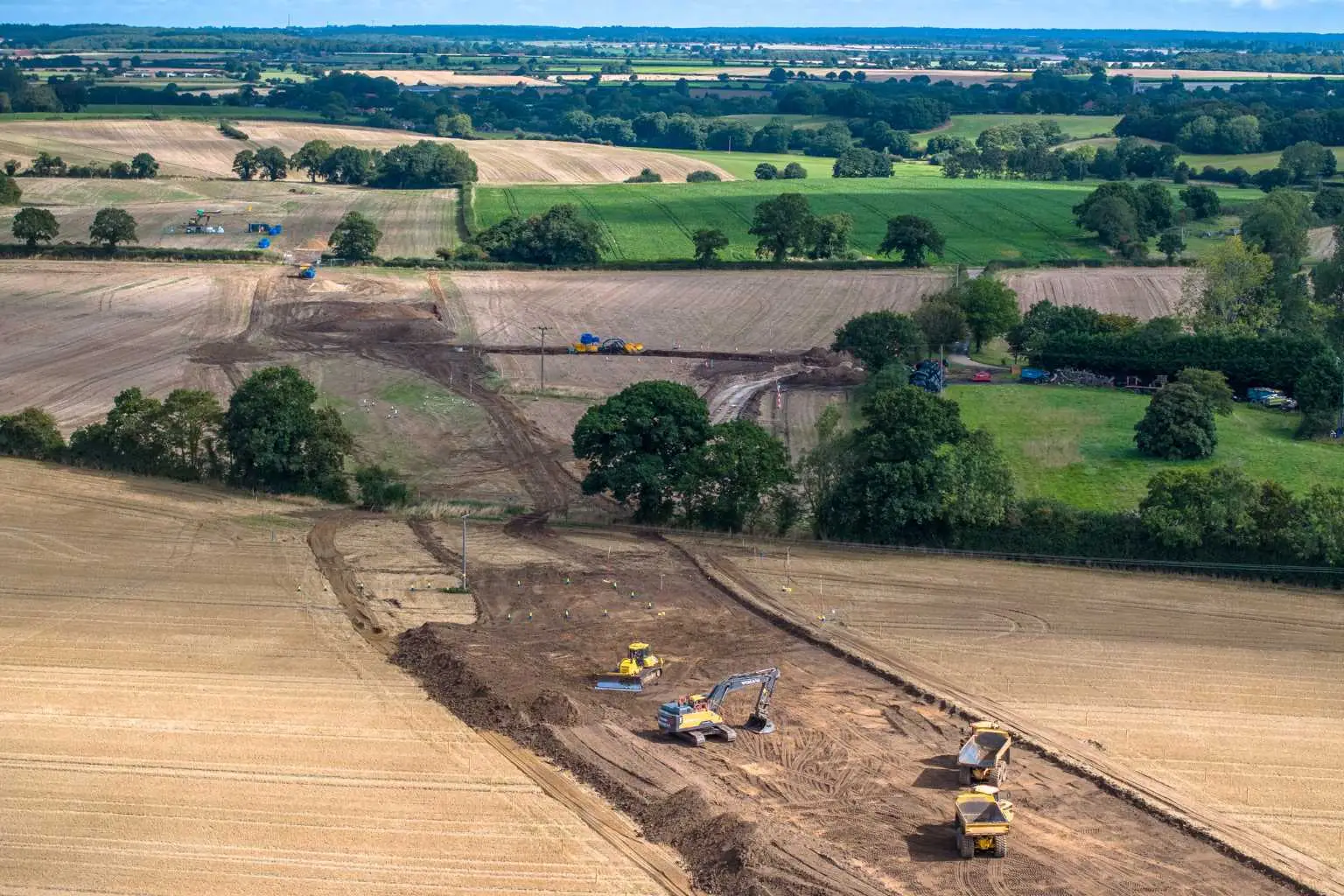 Aerial view of agricultural land showing utility route drainage in action, with heavy machinery used